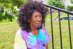 Homeless Woman of Color - African American - Sitting on stairs outside full body showing - Wrinkled Face