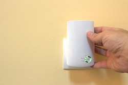 WiFi technology at home, a hand places a white wifi signal repeater into a wall socket
