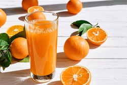 Ripe bio oranges and a glass of fresh squeezed orange juice on white wooden background. Organic Sicilian oranges