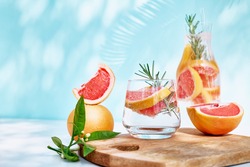 Summer cocktail with grapefruit and rosemary and juicy slices citrus fruits. Fresh healthy grapefruit beverage on sunlight with shadows. Creative drink on blue pastel background.