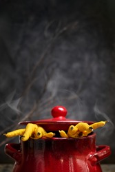 Halloween concept.Two Hen's paws with long nails manicured with black nail polish climb out of a steaming pan on old wooden table on black background with fog and smoke.