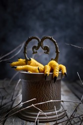 Halloween concept.Two Hen's paws with long nails manicured with black nail polish climb out of the well  on old wooden table on black background with fog and smoke.