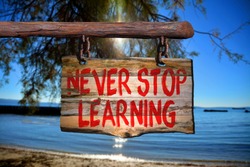 Never stop learning motivational phrase sign on old wood with blurred background