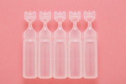 Physiological solution ampoules on pink background, plastic containers with saline serum for cleaning baby skin