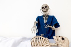 Skeleton doctor wearing blue scrubs uses stethoscope to examine patient lying on hospital bed with shocked and horror look on face after dying waiting for medical care