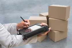 Closeup shooting hand of QC. worker with Rugged computers tablet and Bluetooth barcode scanner checking for logistics, Goods package boxes in warehouse.