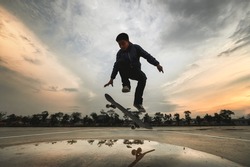 Asian Kids Jumping Tricks - ollie while Skateboarding on-street parking during sunset time., Backlight dark Skateboarder silhouettes