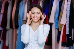 Happy beautiful teenager girl hold hands near face rejoice great good luck in a clothing store. Front view looking at the camera of young girl blows her head from such luck. Young background clothes.