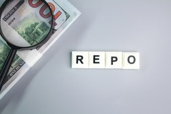 magnifying glass and paper money with the word REPO. REPO stands for Repurchase Agreement.