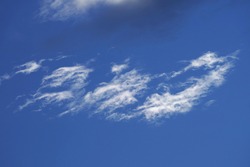 A haze of feather clouds against a bright blue sky. A white cloud is scattered across the sky.