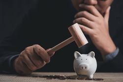 businessman need to use money reserve. man hand smash the piggy bank with a wooden hammer to use the savings. a man smashes his piggy bank on a table.