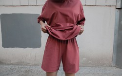 A girl holds a T-shirt from an oversized suit against the wall. Oversized suit. Minimalistic clothing on the model girl. Coral-colored suit. Fashion concept.oversized wear and clothes