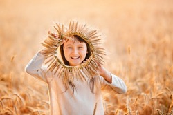A little girl plays with an ear of corn among ripe wheat. The child is cheerful and happy, positive emotions. Wreath of spikelets.