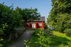 Typical red wooden cottage in Sweden with beautiful garden and a flagpole.