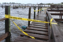Yellow caution tape blocking off access to a public dock at a local marina due to damage from waves crashing in to the wooden dock boards during a bad storm.