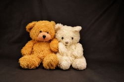 two teddy bears are sitting on a dark background