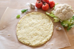 raw pizza base from shredded cauliflower on baking paper, healthy vegetable alternative for low carb and ketogenic diet, copy space, selected focus, narrow depth of field