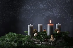 First advent with one burning candle on fir branches with Christmas decoration against a dark grey background, copy space, selected focus, narrow depth of field