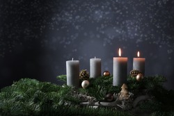 Second advent with two burning candles on fir branches with Christmas decoration against a dark grey background, copy space, selected focus, narrow depth of field