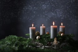 Fourth advent with four burning candles on fir branches with Christmas decoration against a dark grey background, copy space, selected focus, narrow depth of field