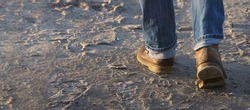 Man walking forward on sand, moving feet with leather boots and rolled up jeans, leisure activity or working concept, selected focus, narrow depth of field