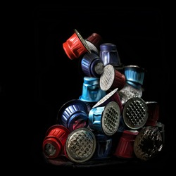 Pile of colorful used coffee capsules against a black background, unnecessary waste from disposable packaging, art concept for environmental protection, copy space, selected focus
