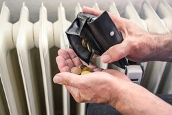 Hands of a man pouring out few coins from a wallet in front of an old heater, suffering from rising energy costs, copy space, selected focus, narrow depth of field