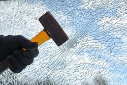 Man’s hand is hitting a window from safety glass with a heavy hammer, vandalism and burglary concept, copy space, selected focus