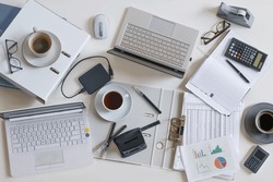 Top view of a full business desk with laptops, accounting papers, calculator, coffee and other office supplies, success work or stress concept, high angle shot from above, selected focus