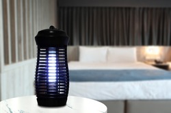 an insects mosquito electric blue light killer lamp is put on the white marble table in the nice bedroom with curtain background to protect the mosquito during sleeping time