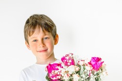 Smiling 8 year old boy with blue eyes holding a bouquet of red and white roses in his hands. Background for a holiday card, copy space