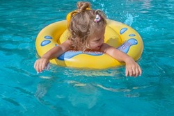 Joyful laughing white caucasian girl 2 years old with blond hair on an inflatable ring while swimming in the pool