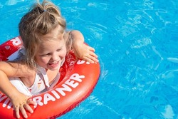 Joyful laughing white caucasian girl 2 years old with blond hair on a red inflatable ring while swimming in the pool