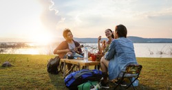 blurry and soft focus of group of Asian friends tourist drinking and playing guitar together with happiness in Summer while having camping near lake at sunset