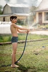 the boys are doused with cold water from a hose. Summer fun in the village, happy kids fooling around and laughing
