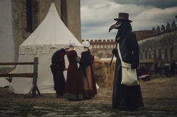 A masquerade historical scene reconstruction. Plague doctor in medieval old town. Castle and epidemic