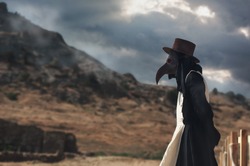 A man in historical masquerade costume of plague doctor in old grange castle near the mountains. Epidemia protection costume. Pandemia horror mystical fantasy plague doctor