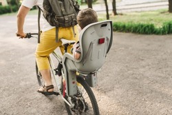 A young father carries his little son in a bicycle seat. dad and son ride a bike. Child safety concept