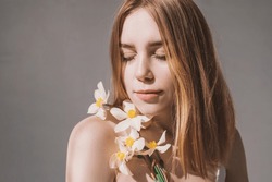 Portrait of a pretty red-haired girl with freckles in flowers with hard shadows and bright sunbeams. Natural beauty without retouching. Self acceptance and caring for your body