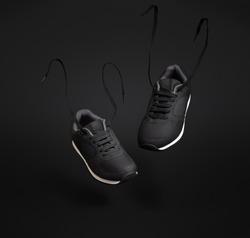 A pair of black unbranded sneakers floating in front of dark background.