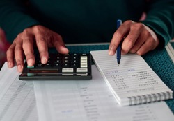 A South Asian man calculating monthly household expenses. Cost reduction, budget and financial planning concept, selective focus on the hand.