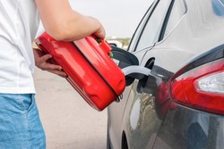 A man pouring gasoline into an empty fuel tank from a plastic red  gas can. Filling  the car from the canister into the neck of the fuel tank. 