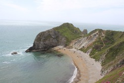 Landscape view of cliffs in Dorset by a sandy beach. The cliffs are covered in grass