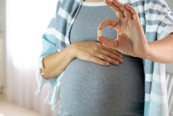 Pregnant woman at home hold pill in hand. Baby expectation, health care and prenatal vitamins on pregnancy time. Illness and medicine while pregnancy.