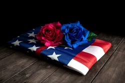 FOLDED FLAG OF THE UNITED STATES OF AMERICA WITH TWO ROSES, ONE RED AND ONE BLUE. HONORS AND MILITARY TRIBUTE TO THE FALLEN SOLDIERS.
MEMORIAL DAY CONCEPT.
