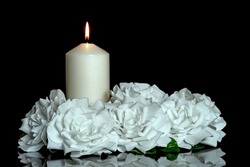 LIGHTED CANDLE AND ELEGANT WHITE ROSES ARRANGEMENT ON DARK BACKGROUND. ALL SOULS DAY, DEATH, DECEASE, PRAYER, MEMORIAL DAY, DUEL, MOURNING, GRAVE, CEMETERY, BURIAL, CONDOLENCE AND FUNERAL CONCEPT.