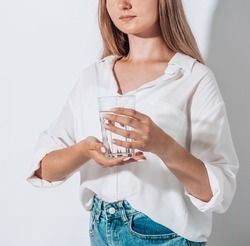Girl drinks water ffrom a glass cup on a white background. The concept of maintaining water balance