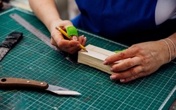 A female carpenter marks details with a pencil and cuts wood with a knife in a carpentry or homemade workshop. Dust and dust are flying in the air.Workplace. Production of wooden toys.