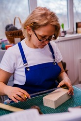 A female carpenter measures details and cuts wood with a knife in a carpentry or homemade workshop. Dust and dust fly in the air.Workplace. Production of wooden toys.