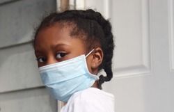 Girl Wearing surgical mask standing on house back porch with white door